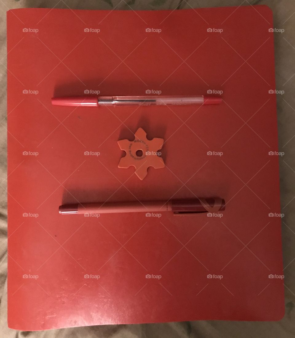 Two red pens and a red eraser on a red binder. All four stationary items go well altogether.