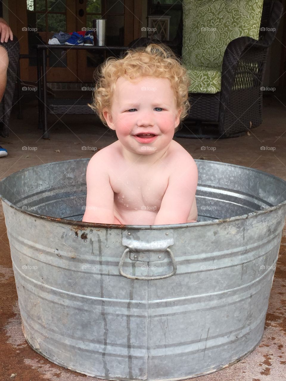Beautiful red headed naked baby taking a bath in a metal tub on a warm summer day