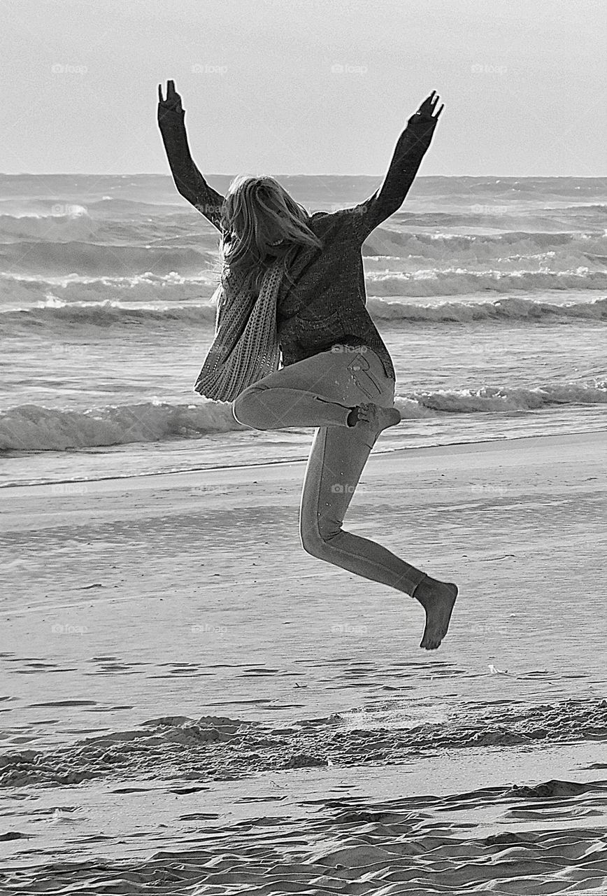 Glimmers: Small Moments of Happiness  - Black and white photo - A girl jumps for joy while on the sandy beach of the Gulf of Mexico 