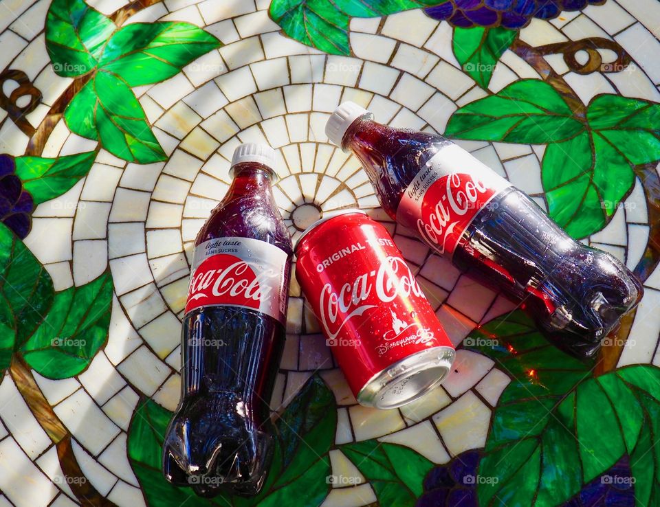 Two Diet Coke bottles and a coke can on garden table.
