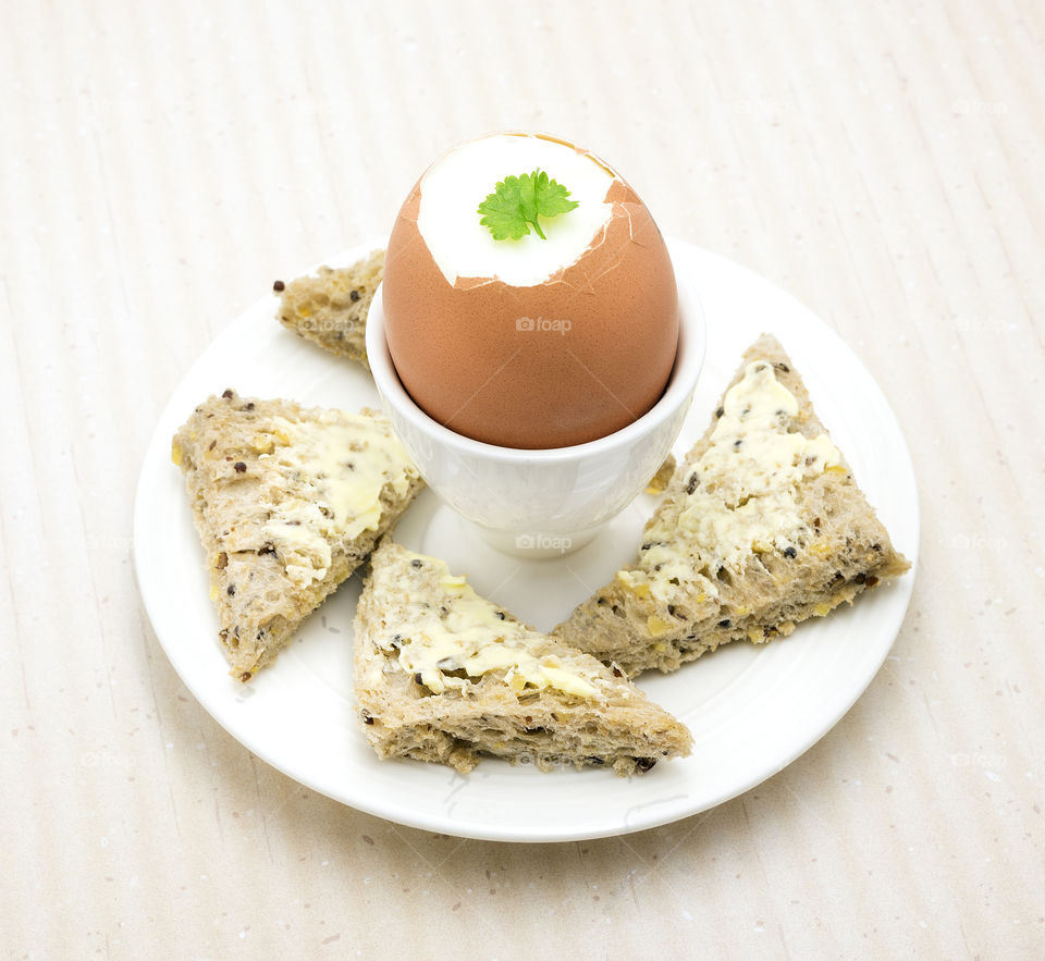 A healthy breakfast to start the day. A hard boiled egg in a white egg cup and triangles of wholegrains bread.