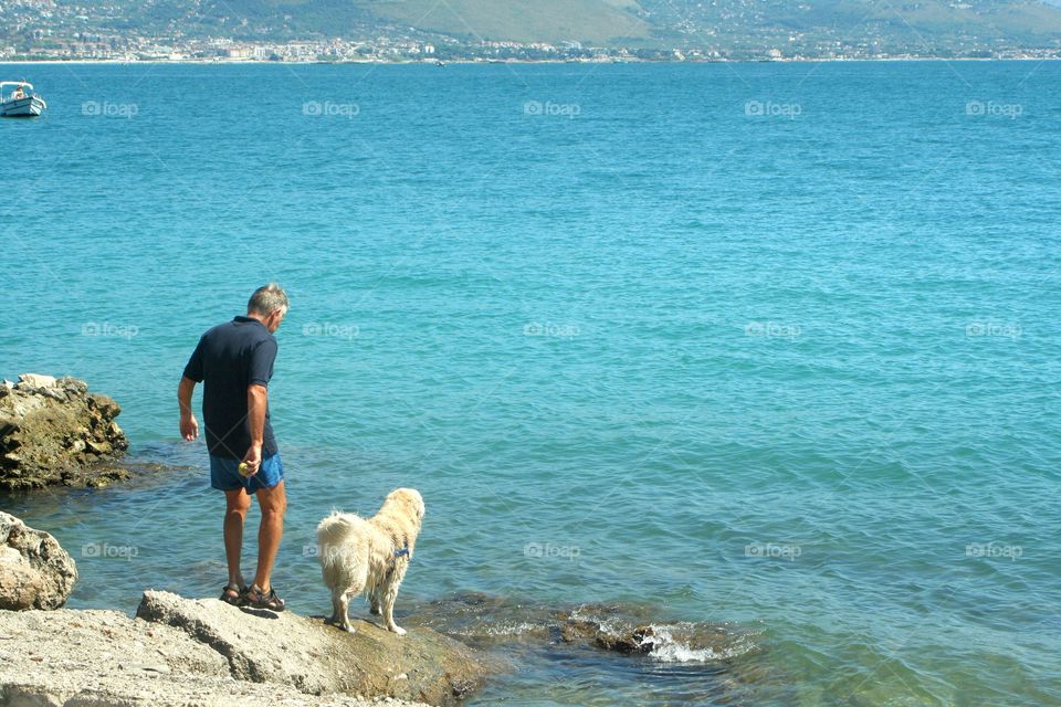 Scenic dog and man on rocks in front of sea