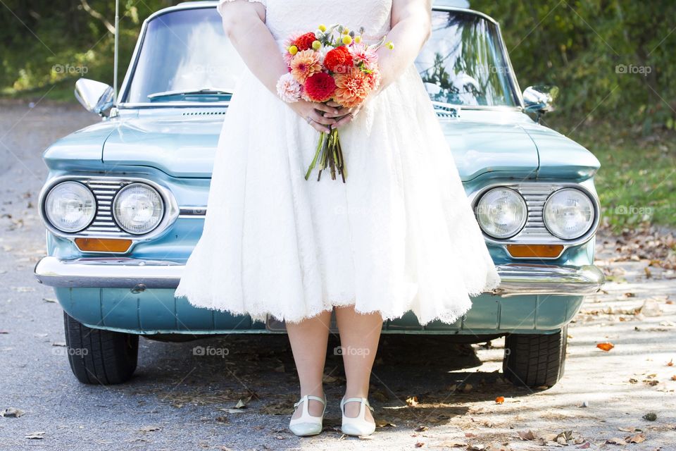 Woman in wedding dress standing against car