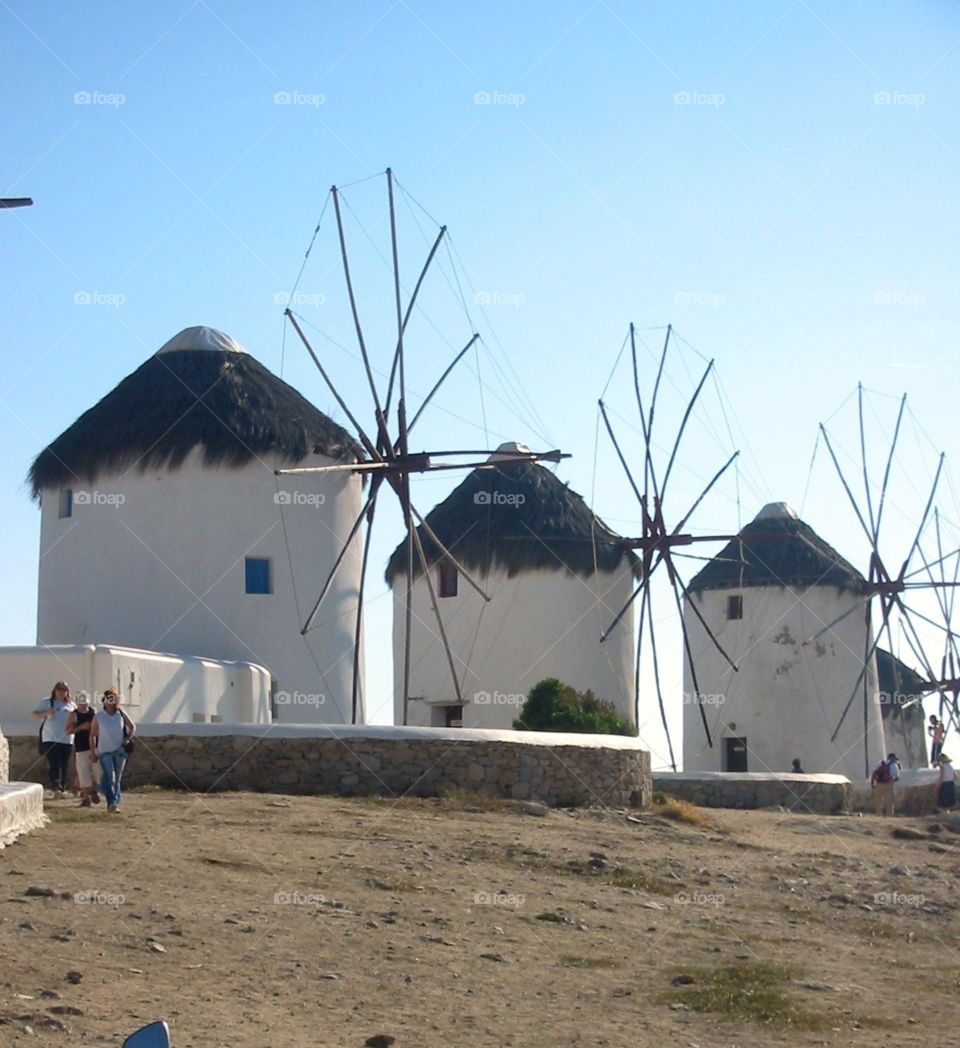 Trio of traditional windmills off Little Venice rolling hills in Mykonos, Greece under the bright blue sky