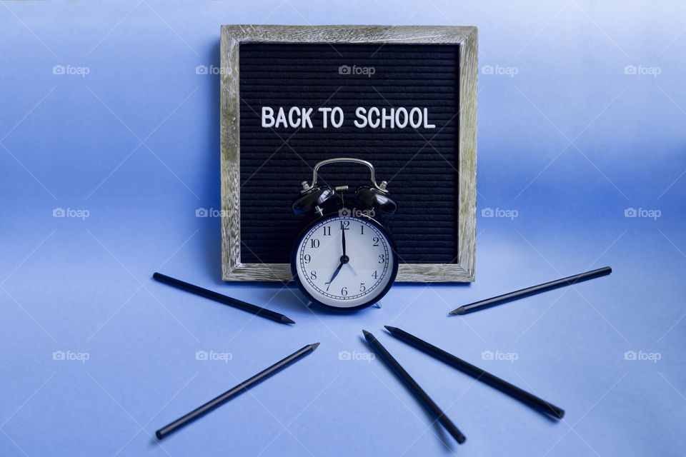 Back to school concept. Alarm clock set to 7am and pencils on blue background.