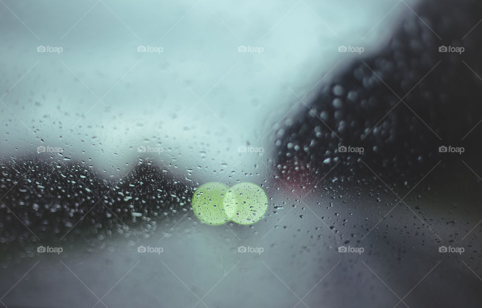 Raindrops and traffic lights seen through windshield during rain.