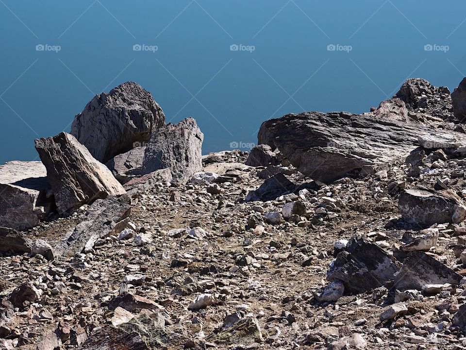 Jagged rocks and boulders along the shoreline of Ochoco Lake in Central Oregon on a sunny spring day.