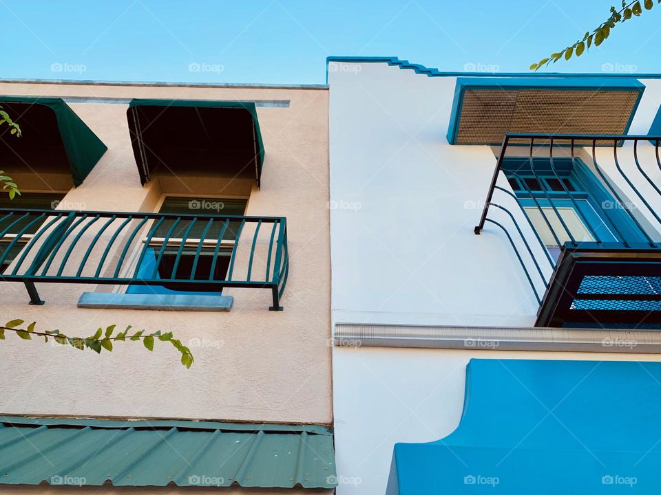 Architectural series of blue, white, green and beige historical building in downtown central eastern Florida town with European style with awnings, balconies, tropical trees and blue sky low angle and seems symmetrical.