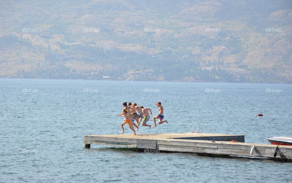 Group of young people jumping in lake together