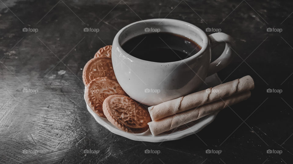 A cup of black coffee with biscuits on the floor