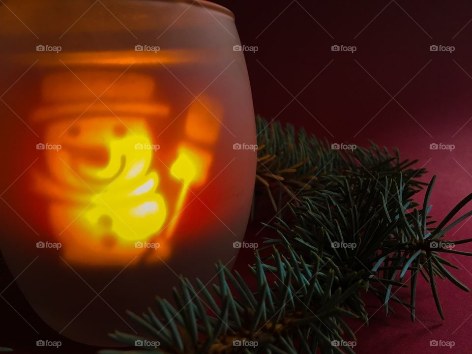 Christmas spirit pictured through lit up snowman candle and pine tree branches. 