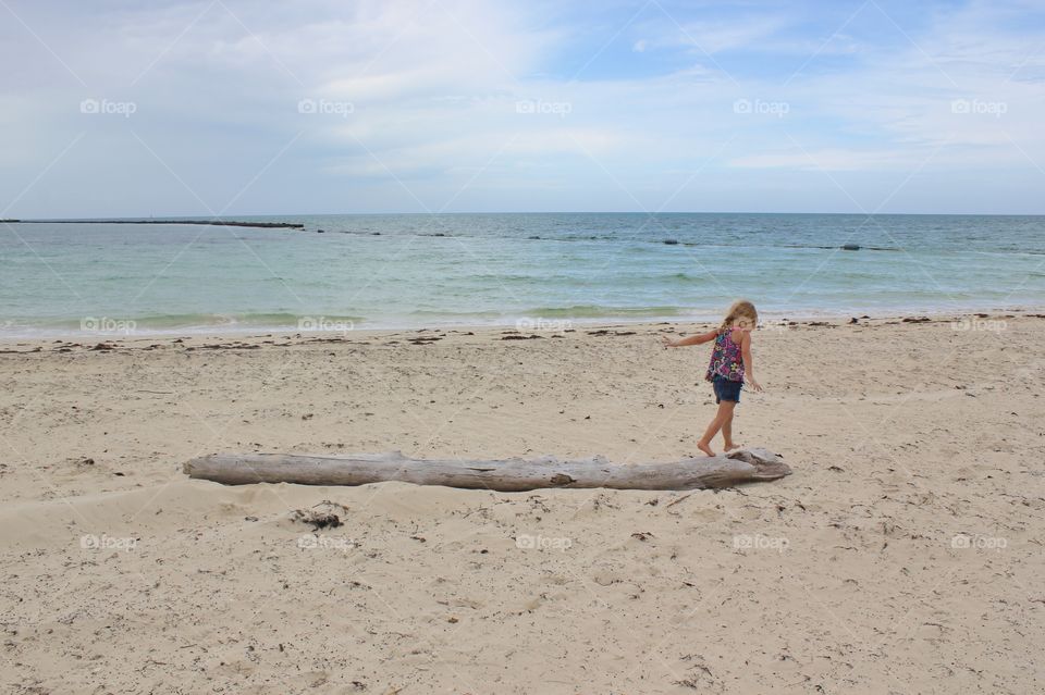 Little girl balancing on driftwood at the beach 